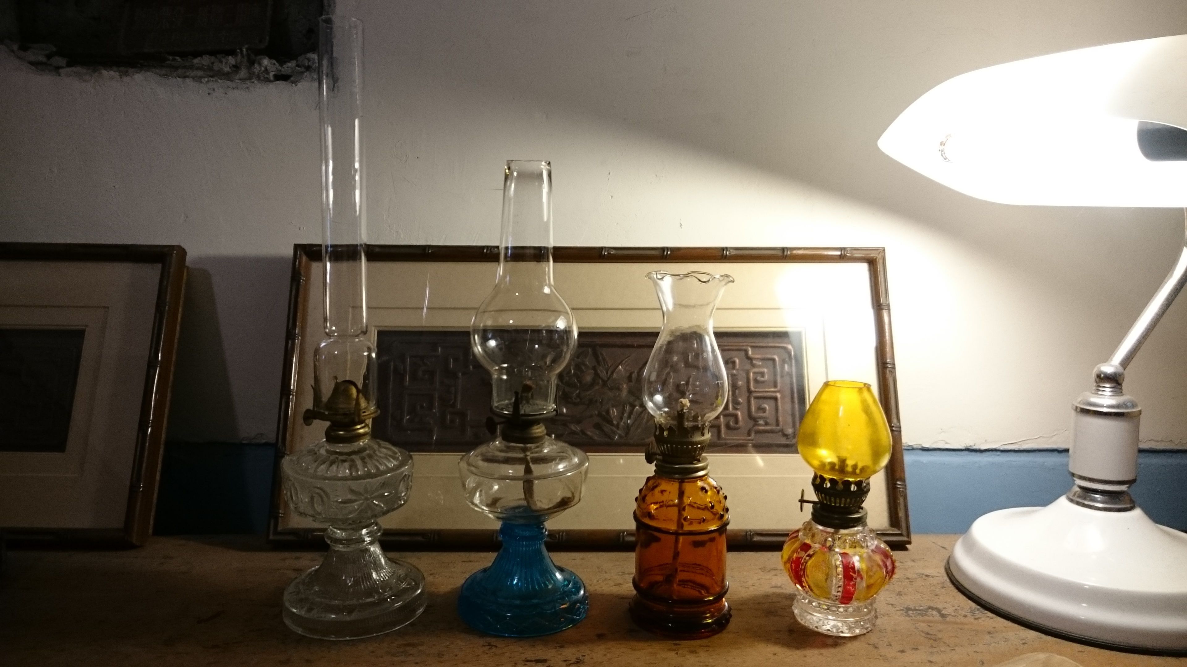 Four glass lamps with different colored bases on a table, a framed picture in the background, and a white table lamp to the right.
