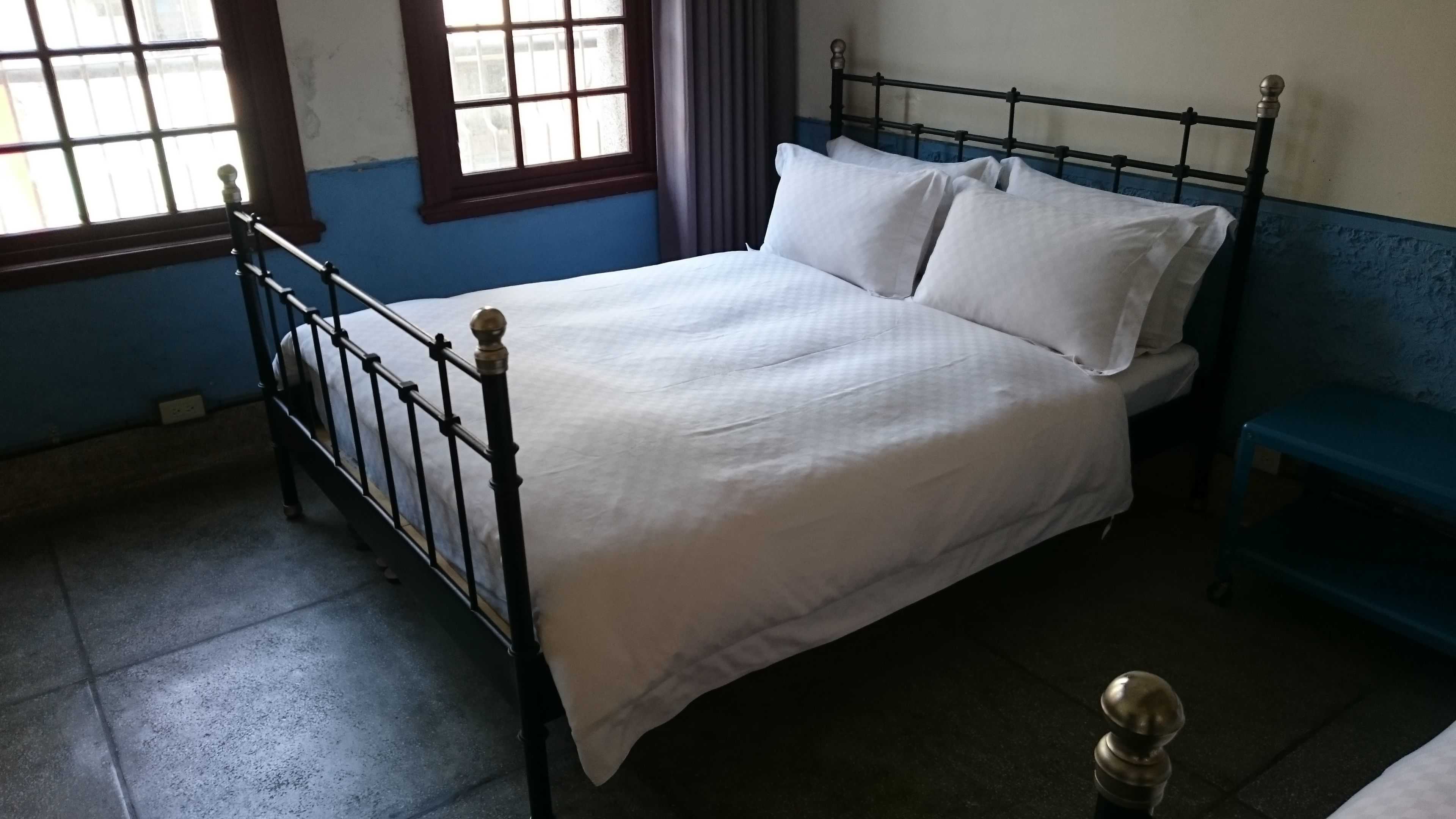 A single bed with a metal frame and white bedding in a room with blue walls and a window.
