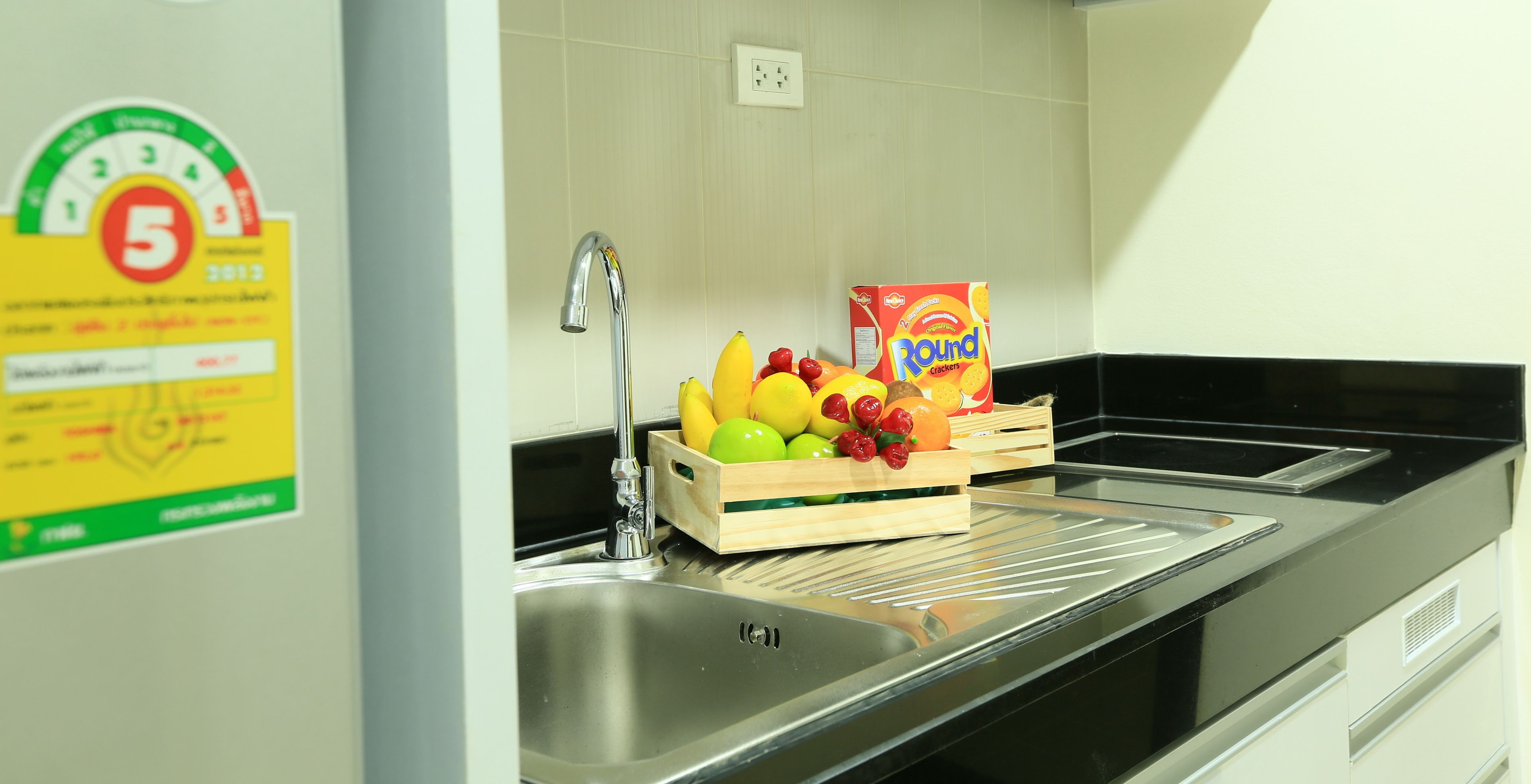 A kitchen with a stainless steel sink, a wooden fruit crate with apples and bananas, and a box of Round crackers.