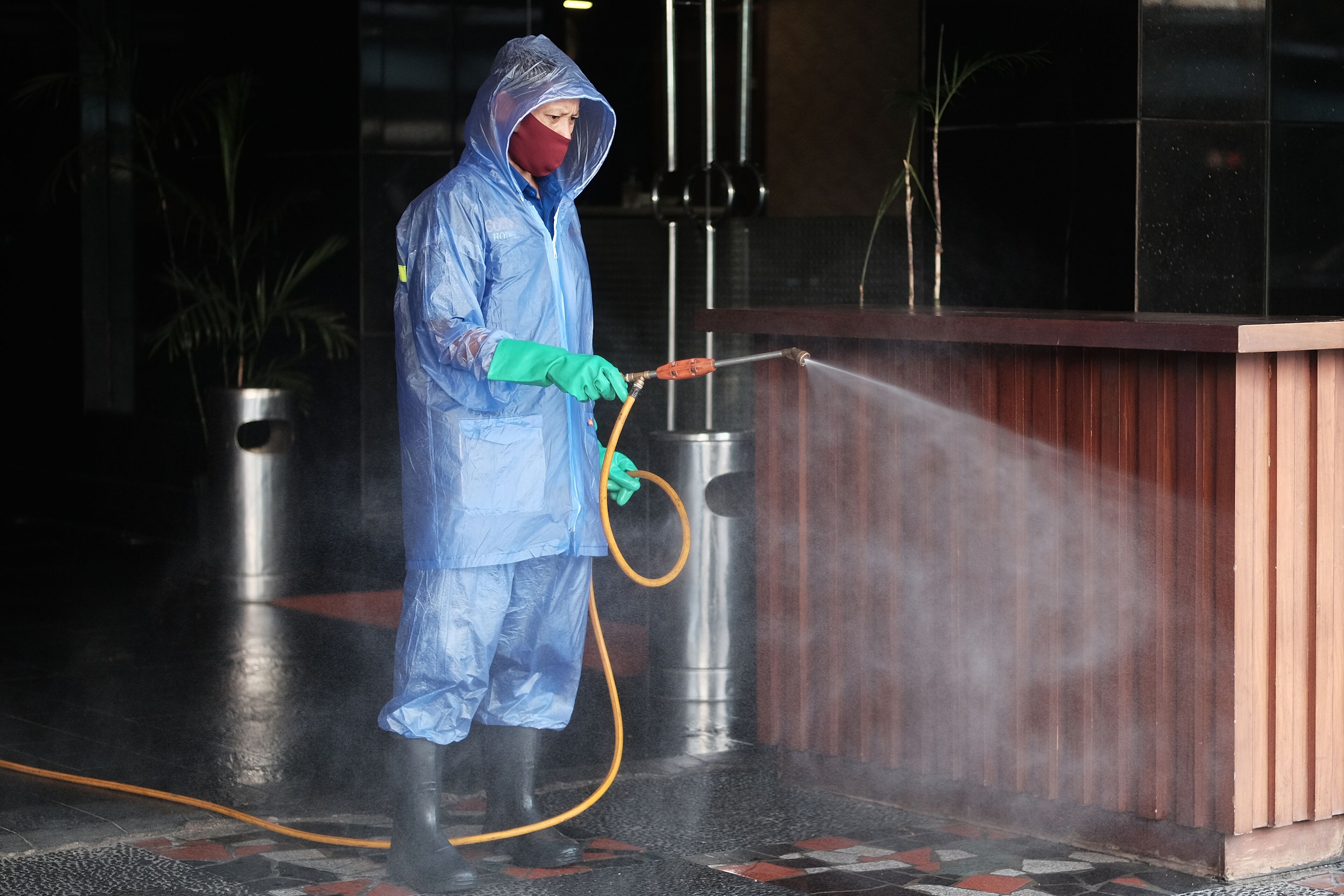 A person in protective gear spraying water on a building's exterior.