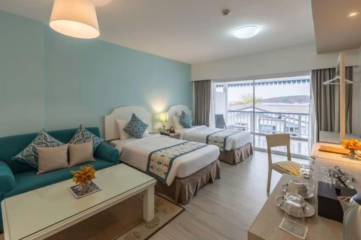 A hotel room with two beds, a sofa, a dining table, and a view of the outside.