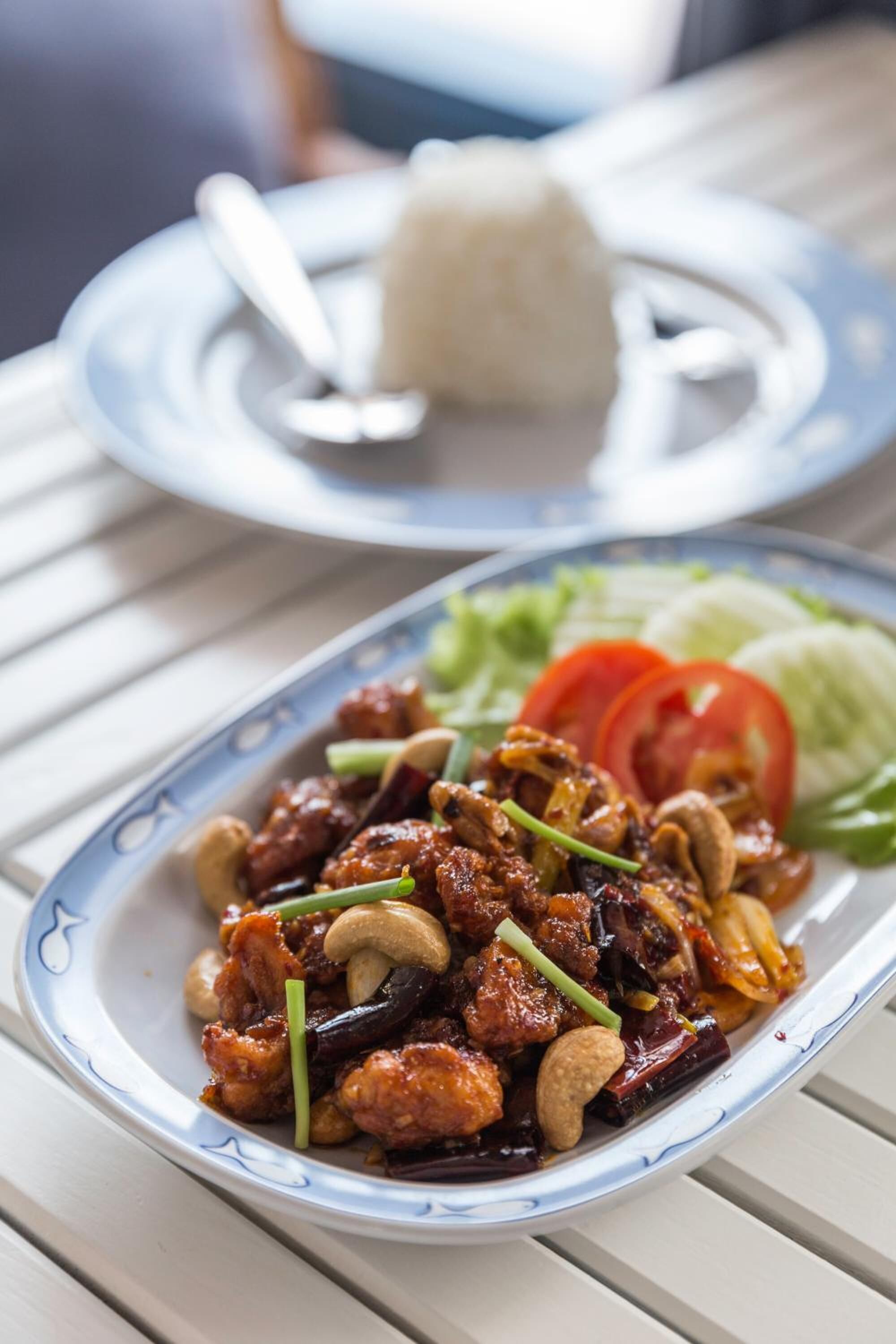 A plate of stir-fried chicken with cashews and vegetables, accompanied by a bowl of rice and a side salad.