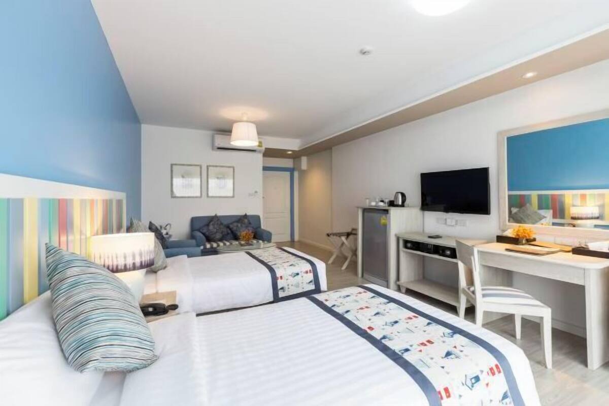 A hotel room with two beds, a desk, a TV, and a kitchenette.