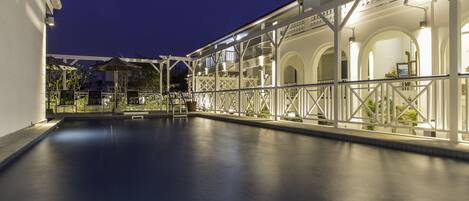 A swimming pool area with a covered walkway and a building with arched windows.