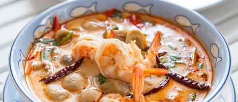 A bowl of soup with shrimp and vegetables, served on a white plate with a blue rim.