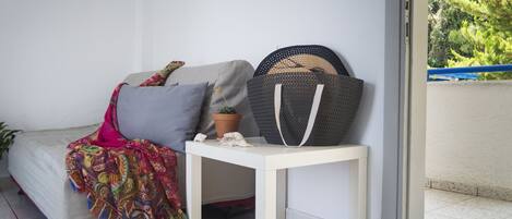 A room with a bed, a small table with a basket, a potted plant, and a view of greenery outside.