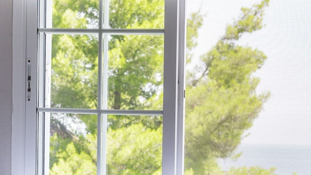 A bed with white bedding and a view of trees through a window. - Roditsa Patritsia Apartments (Kassandra)
