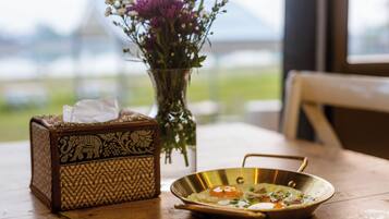 A wooden table with a tissue box, a vase with flowers, and a metal bowl with food.