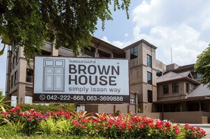 Et skilt med teksten 'BROWN HOUSE' og kontaktoplysninger, placeret foran en bygning med flere etager og altaner.