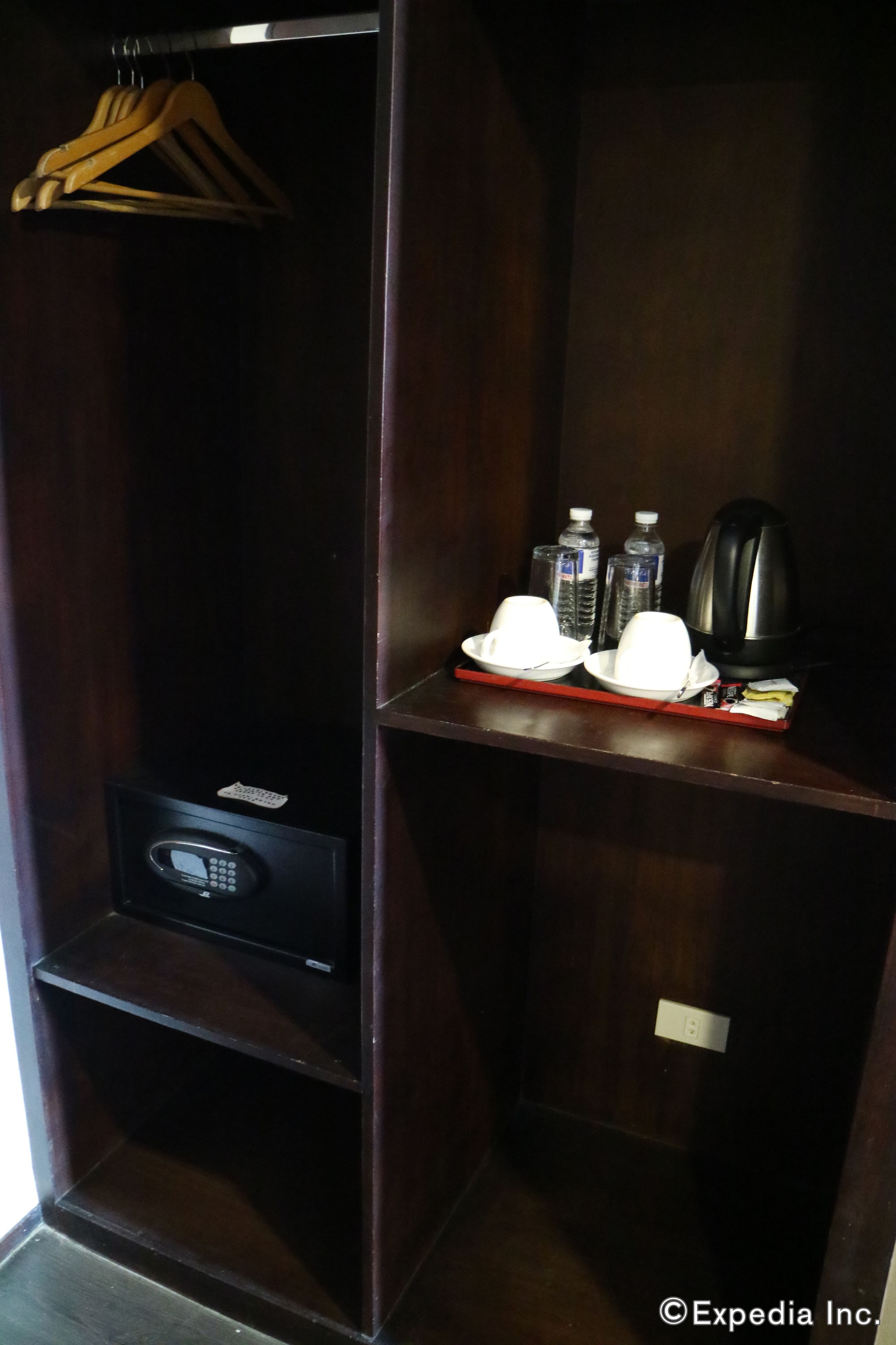 A dark wooden closet with a shelf containing a white hat, a black electronic device, and two water bottles.