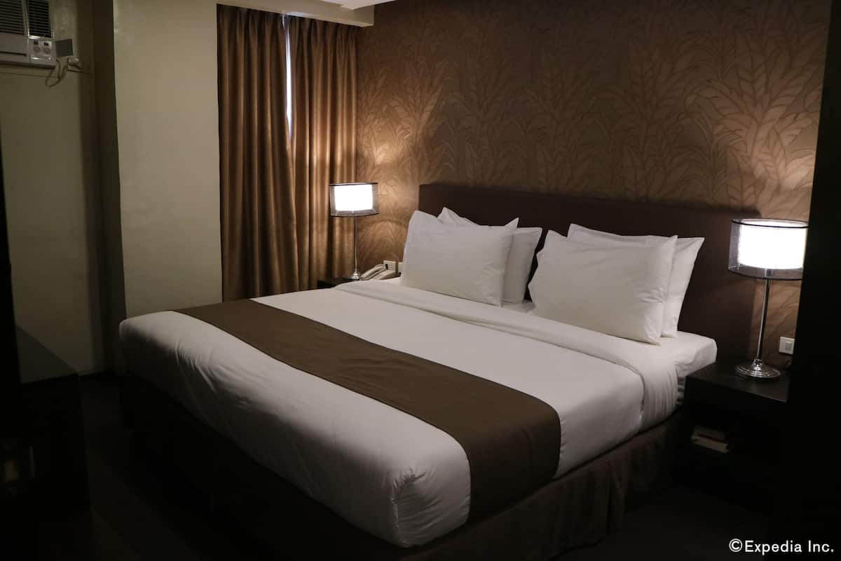 A hotel room with a large bed, two bedside lamps, a telephone, and a wall-mounted air conditioning unit.
