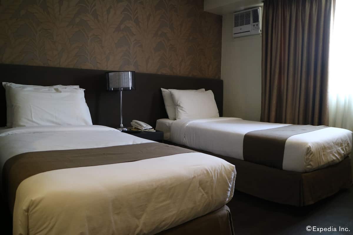 A hotel room with two beds, a nightstand with a lamp, and a phone.