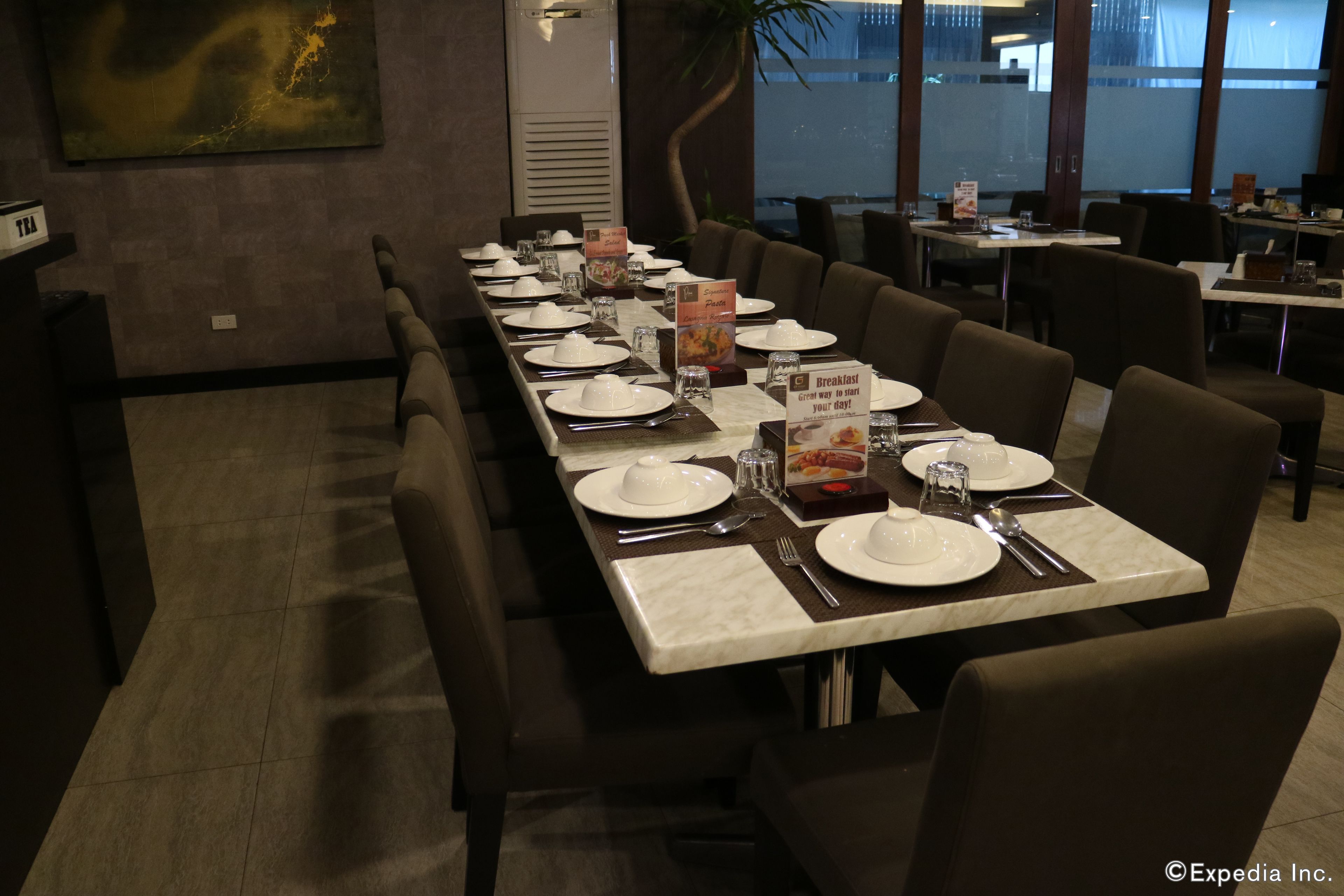 A long dining table set with white plates, silverware, and glassware, with menu cards and a sign indicating breakfast options.