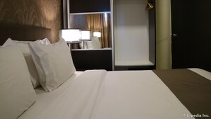 A hotel room with a neatly made bed, a bedside table with a lamp, a wardrobe, and a mirror. - GT Hotel Iloilo (Iloilo)