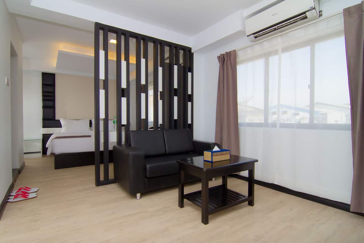 A modern living room with a black sofa, a small table, and a large window with curtains.