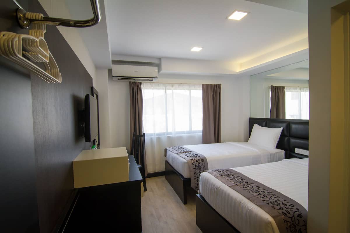 A hotel room with two beds, a desk, a chair, an air conditioning unit, and a large mirror.