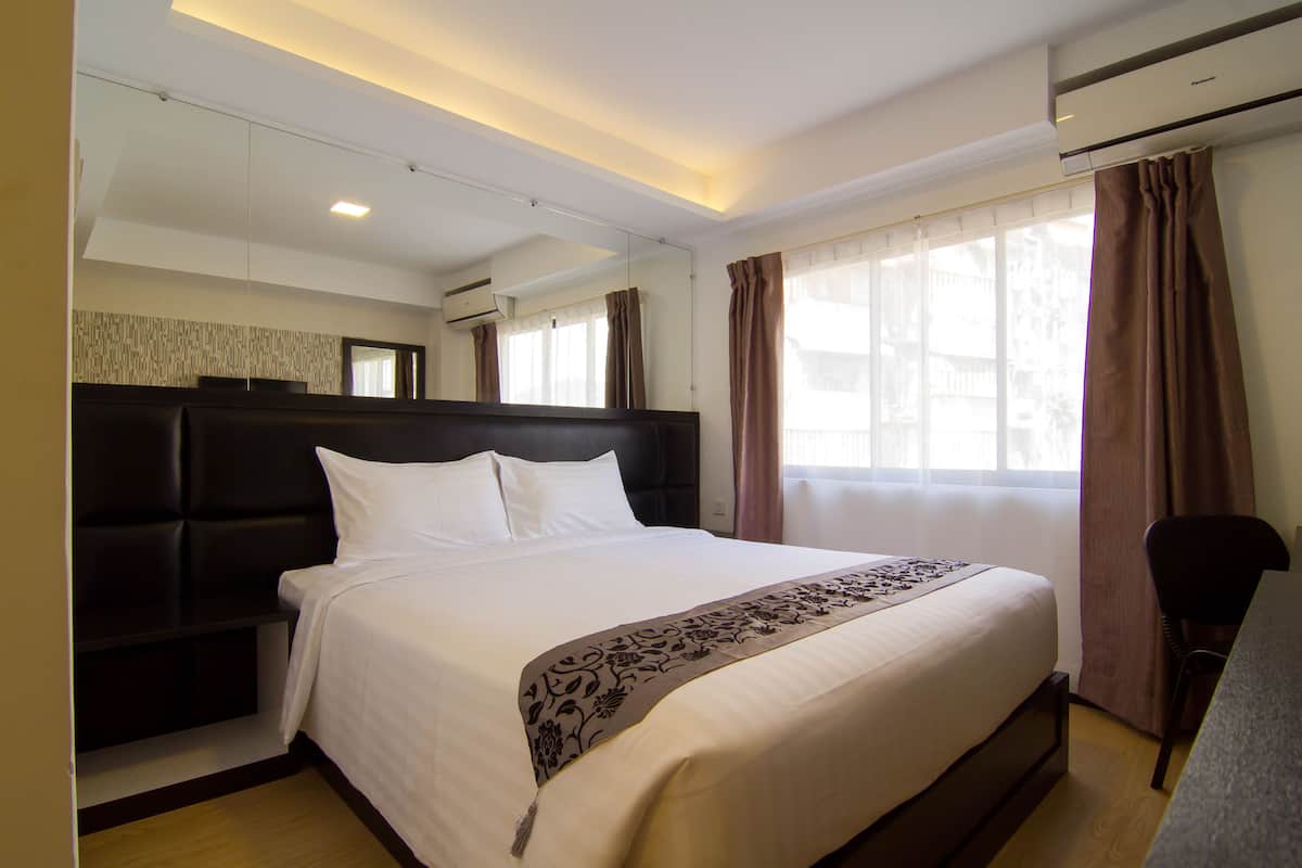 A hotel room with a large bed, a headboard, a desk, and a window with curtains.