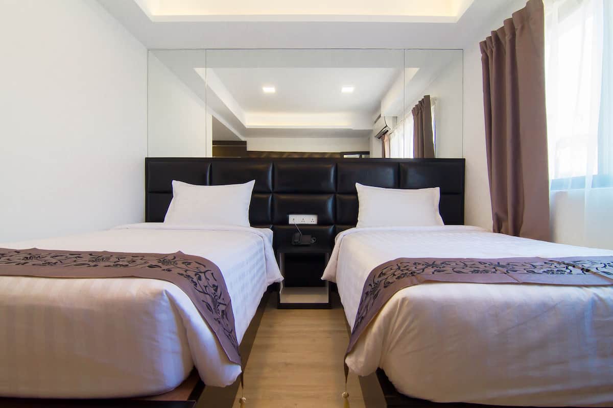 A hotel room with two beds, a dark headboard, a mirror, and a window with curtains.