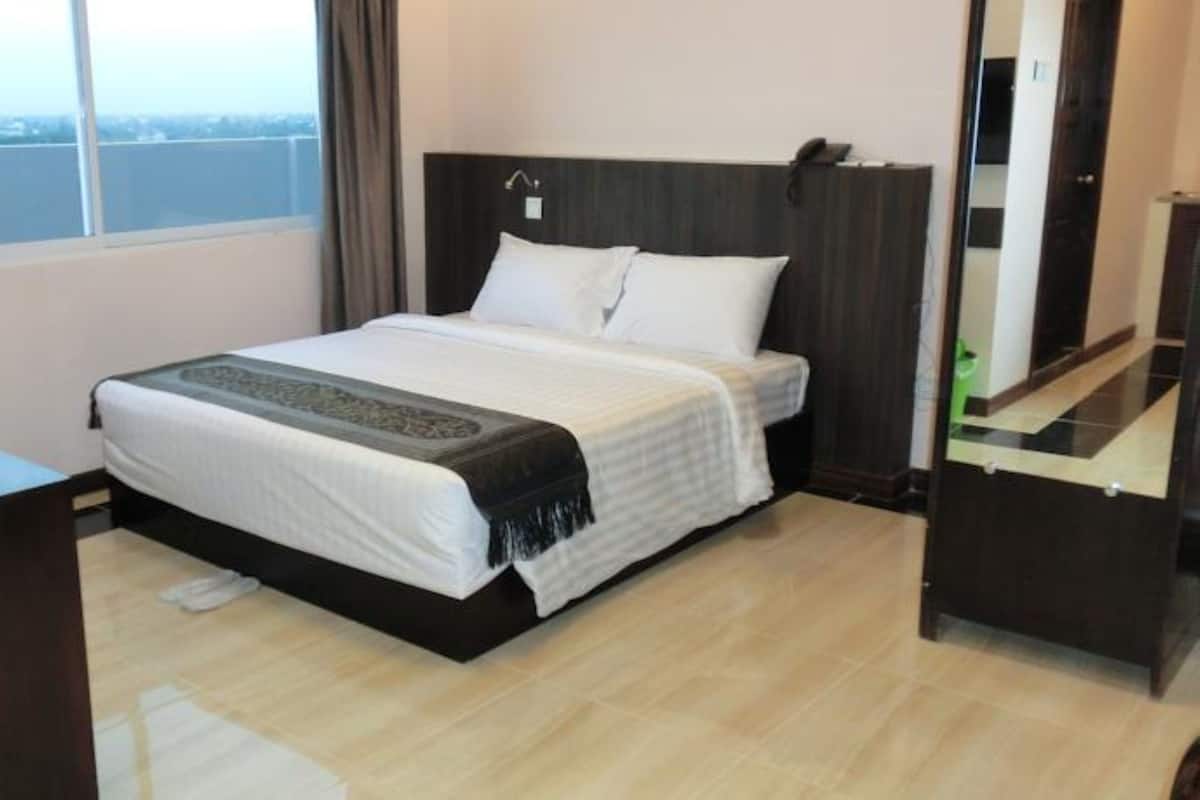 A hotel room with a bed, a TV, a window with a view, and a mirror.