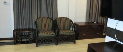 Une pièce comprenant deux chaises à rayures, une petite table ronde, un meuble en bois et un téléviseur posé sur un meuble.