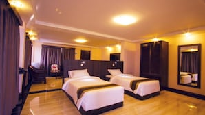 Habitación de hotel con dos camas individuales, un espejo grande, piso de madera y una silla con cojín floral.