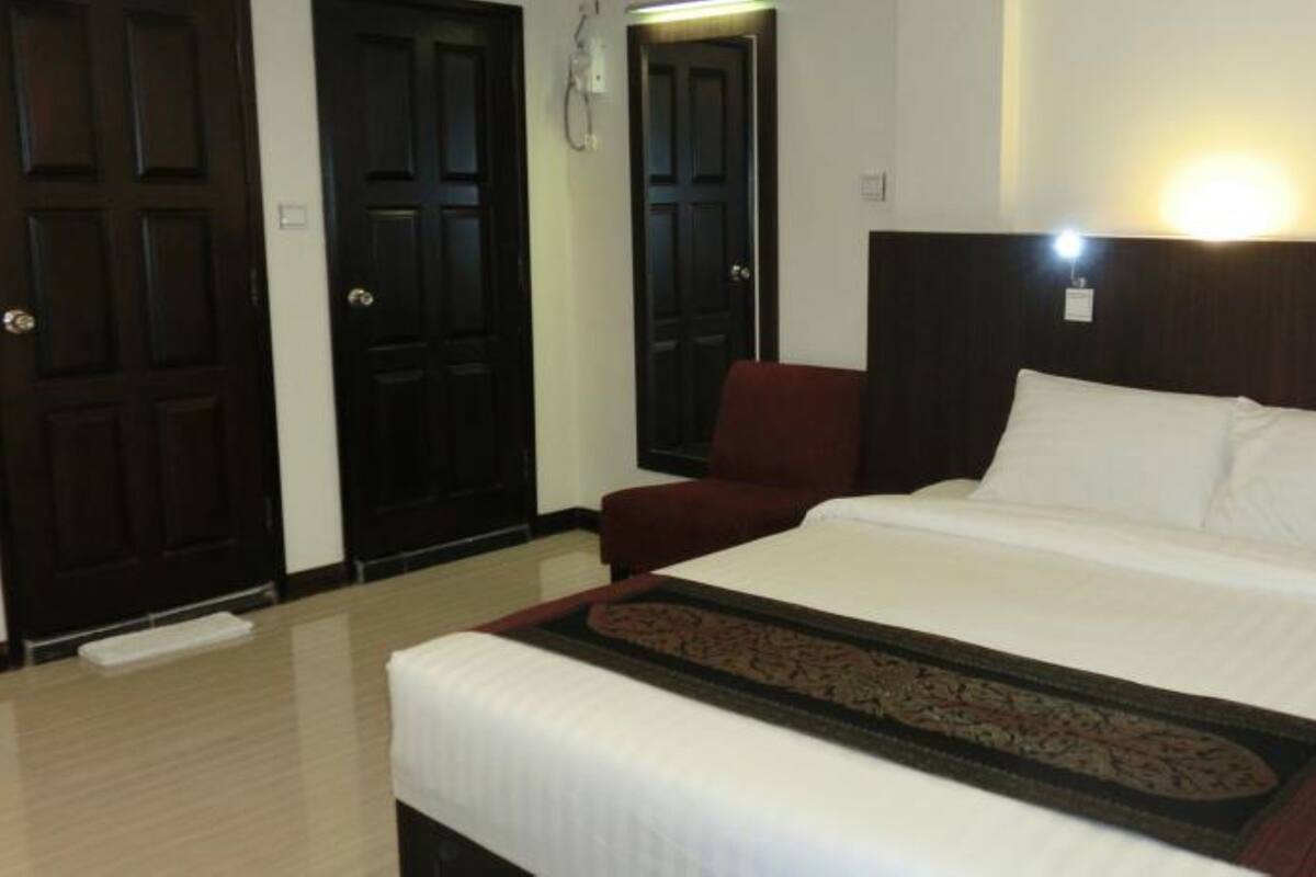 A hotel room with a large bed, a red armchair, and two dark wooden doors.