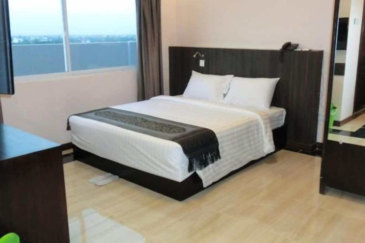 A hotel room with a bed, a desk, and a window.