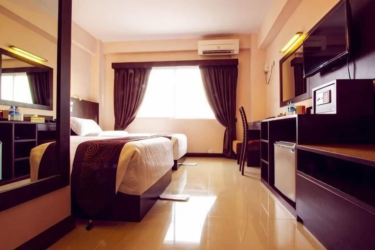 A hotel room with a bed, a desk, a chair, a TV, and an air conditioning unit.