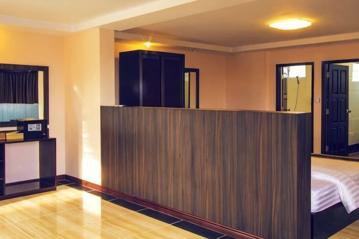 A hotel room with a wooden partition, a bed, a desk with a computer, and a mirror.