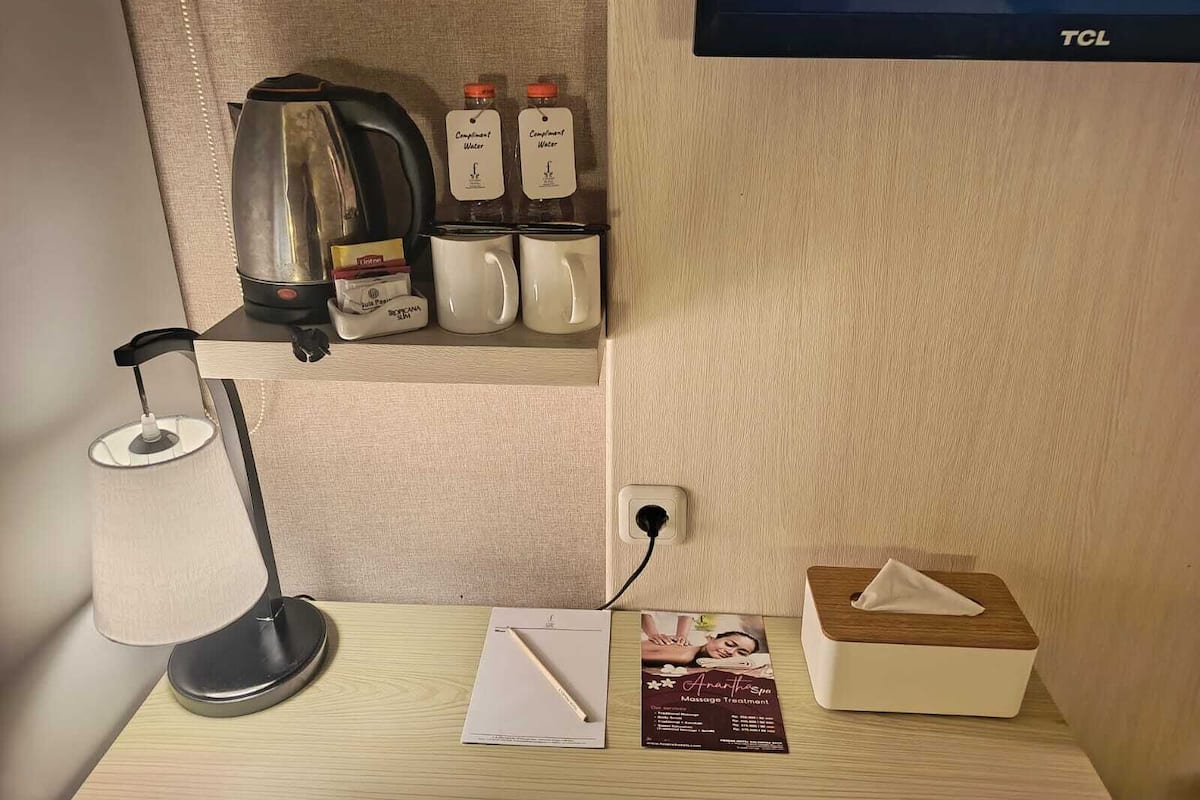 A hotel room with a desk, a lamp, a coffee maker, two bottles of water, a tissue box, and a massage treatment brochure.