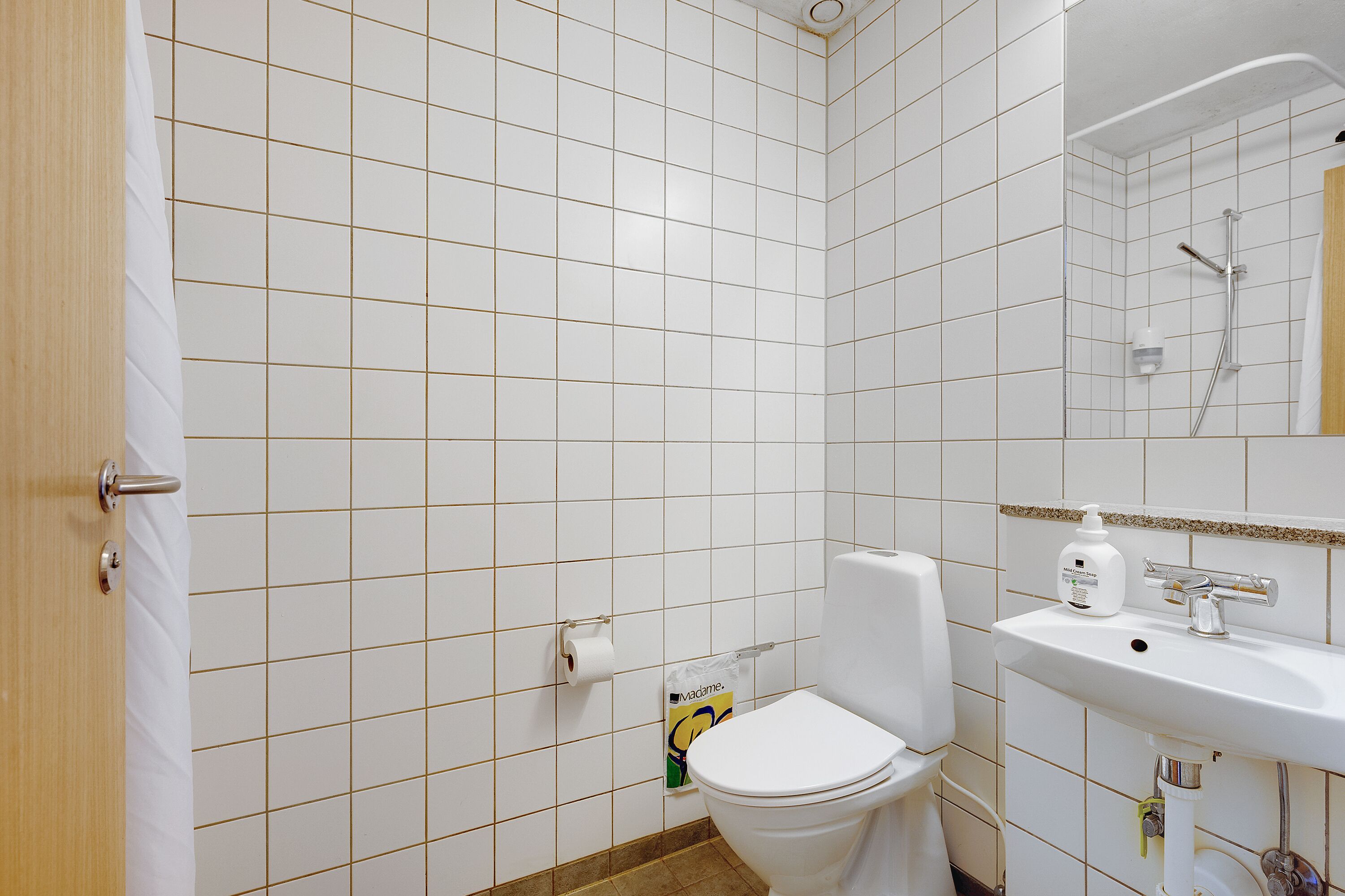 A bathroom with white tiled walls, a white toilet, a sink with a mirror, and a shower.