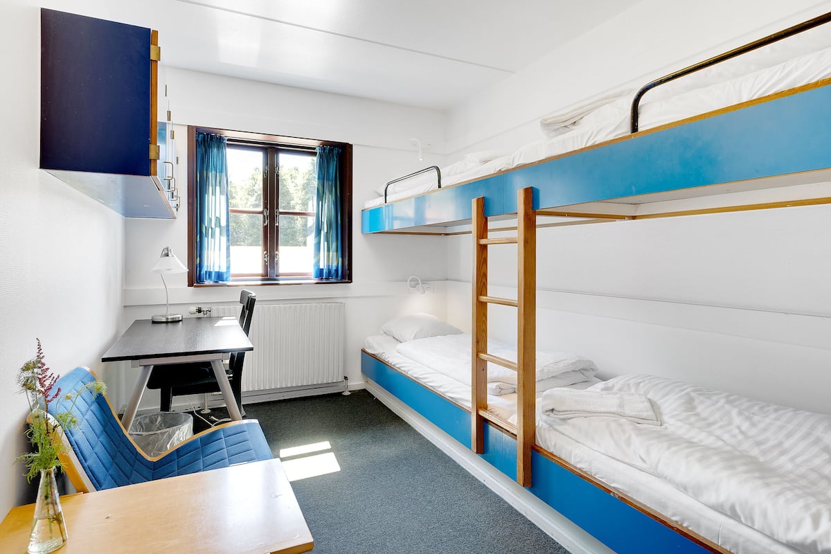 Un dormitorio con literas, un escritorio, una silla, un radiador y una ventana con cortinas.