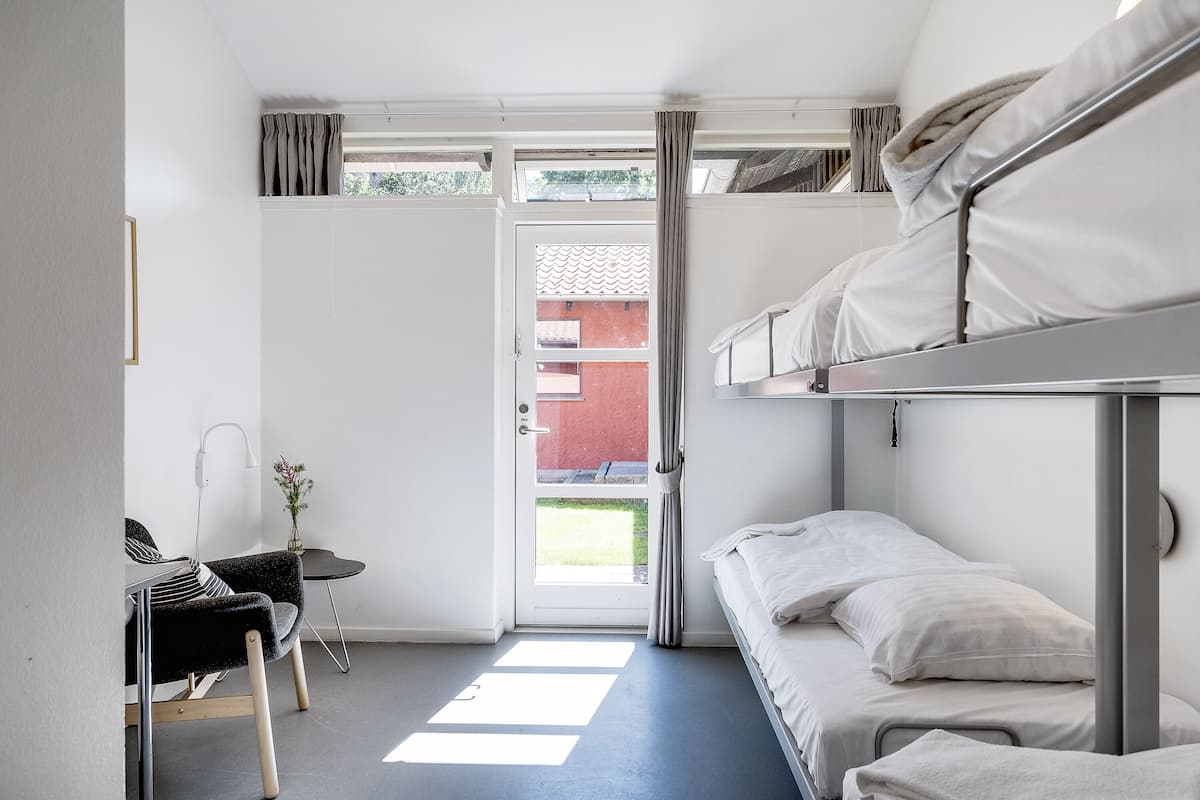Habitación compacta con literas, un escritorio con silla y una mesita con un florero.