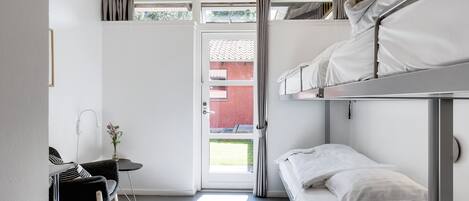 A compact room with a bunk bed, a desk with a chair, and a small table with a vase.