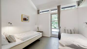Una habitación con dos camas, una mesita con un florero, un cuadro en la pared y una ventana con cortinas.