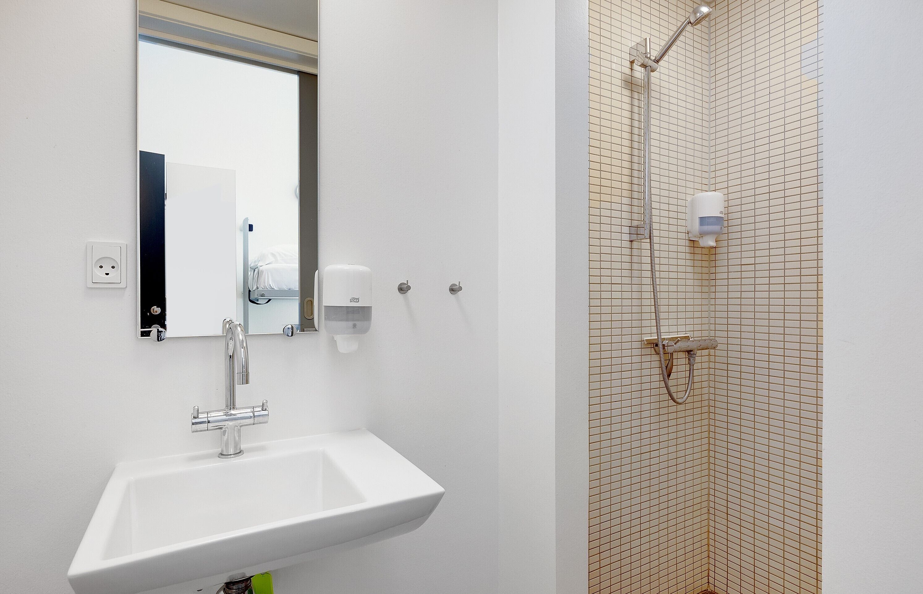 A bathroom with a white sink, a mirror, and a shower with a handheld showerhead.