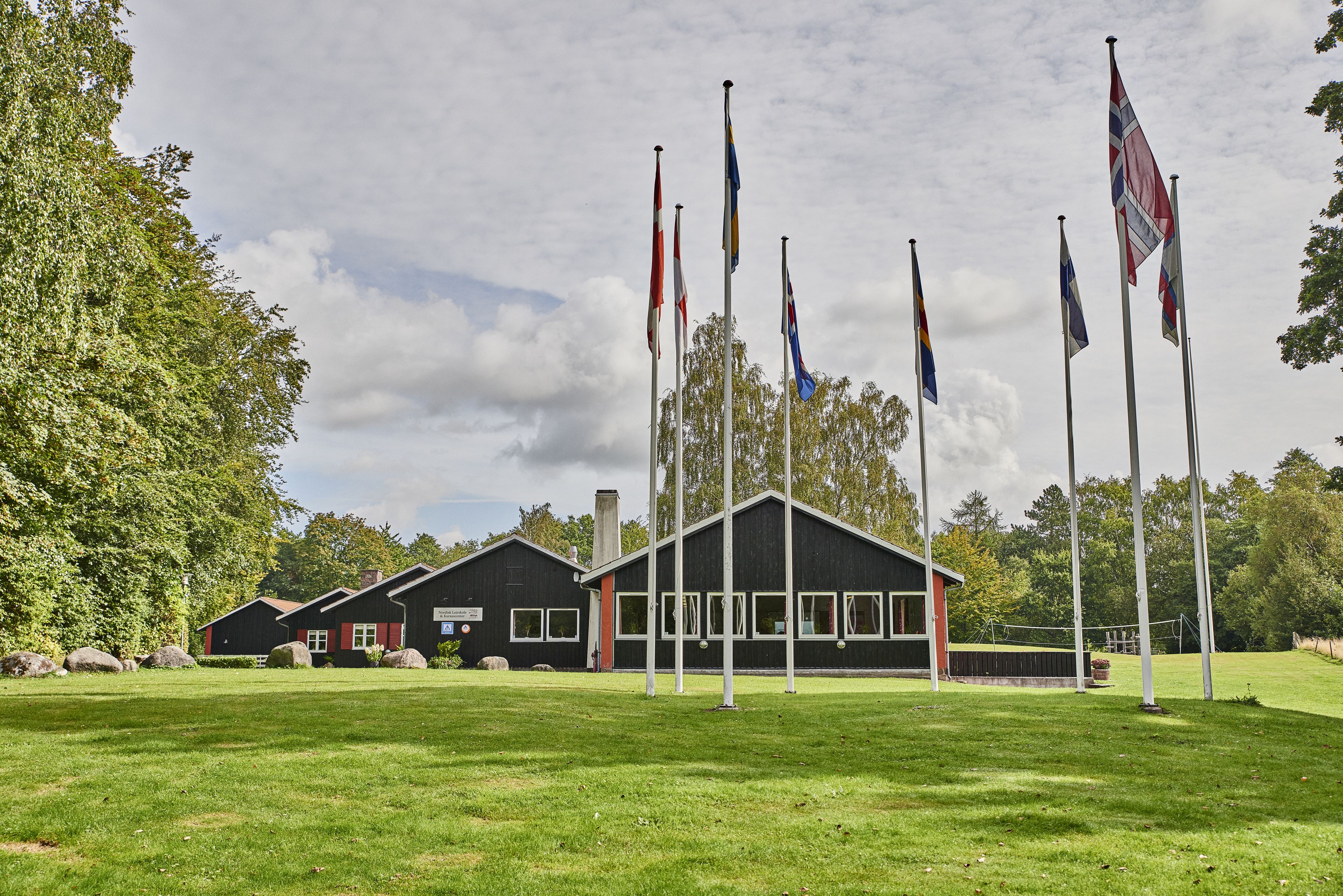A building with multiple flags, a grassy area, and trees in the background.