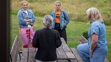 Un grupo de personas sentadas en una mesa de picnic de madera al aire libre, con un campo cubierto de césped y árboles de fondo.