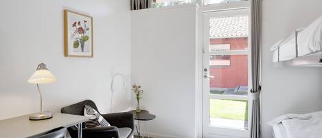 Una habitación con escritorio, silla, cama y una mesita con un florero.