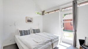 Un dormitorio con una cama grande, una mesita pequeña y un ventanal con cortinas.