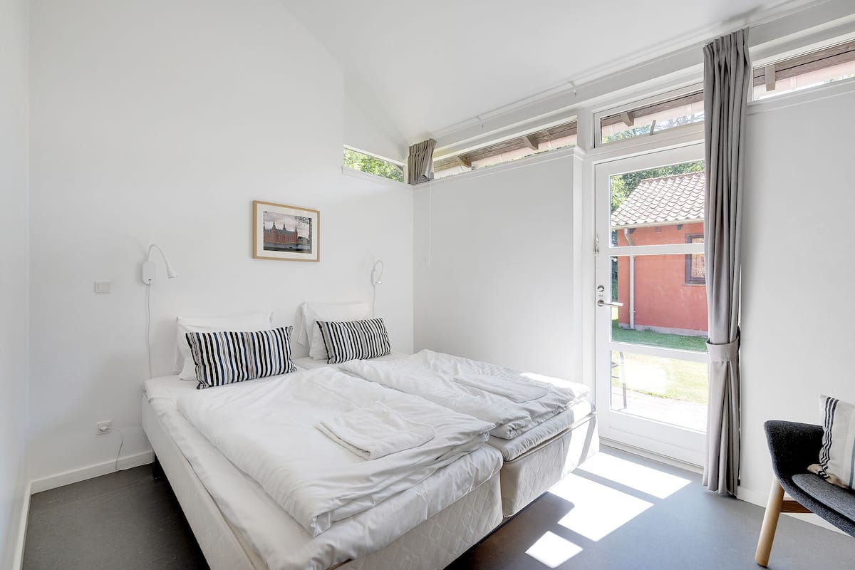 Un dormitorio con una cama grande, una mesita pequeña y un ventanal con cortinas.