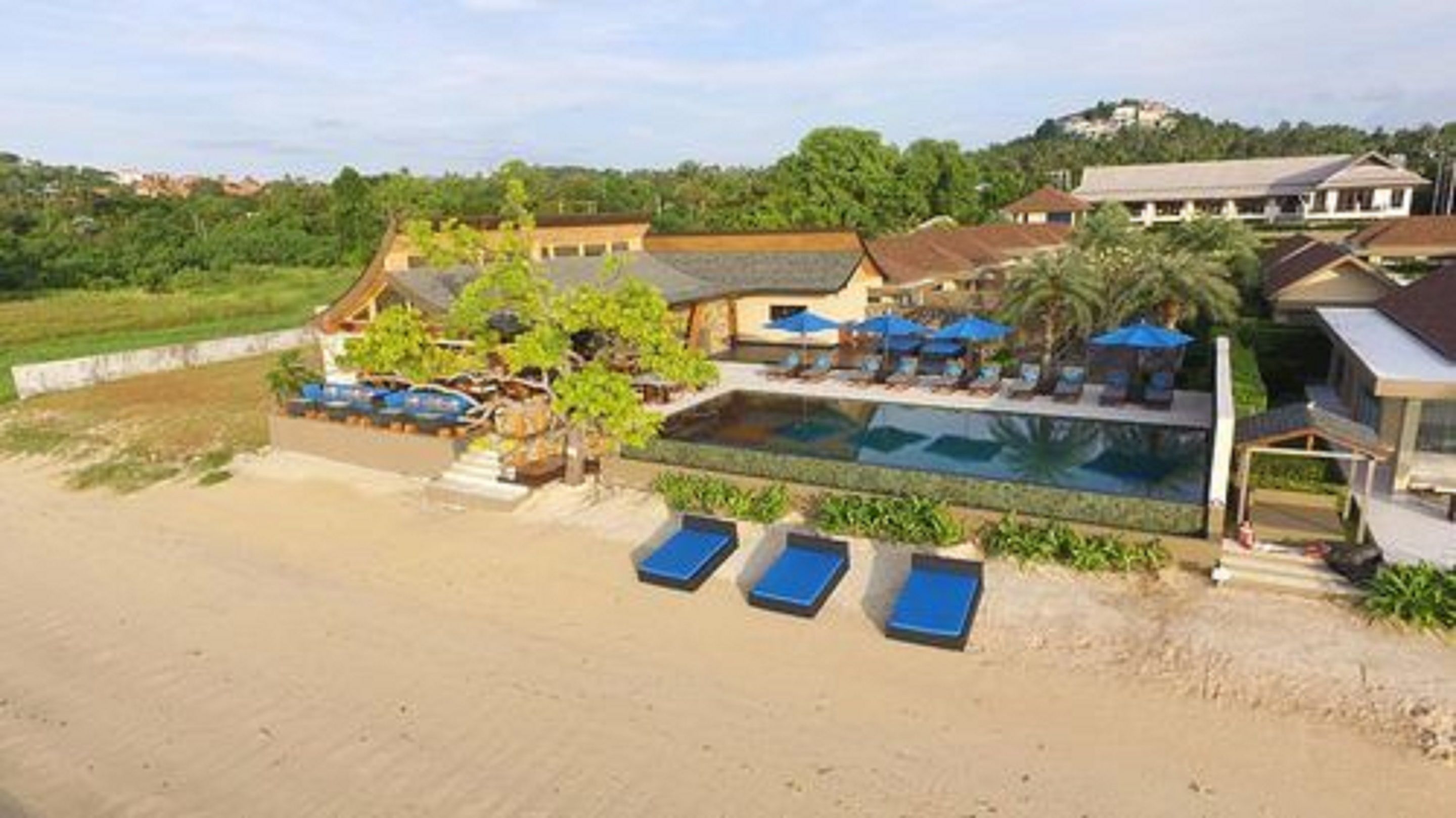 A resort with a swimming pool, lounge chairs, and a beach area.