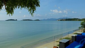 A beachside lounge with a glass railing, blue seating, and a view of the sea and distant islands. - Tides Boutique Samui Resort & Spa (Koh Samui)