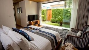 A bedroom with a bed, a TV, and a view of a garden. - Tides Boutique Samui Resort & Spa (Koh Samui)