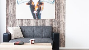Un salon avec un canapé gris, une table basse en bois, un tableau encadré représentant un taureau et un haut-parleur noir.