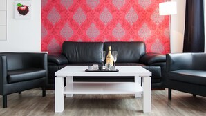 Un salon moderne avec une table basse blanche, des canapés en cuir noir et un papier peint à motifs rouges.