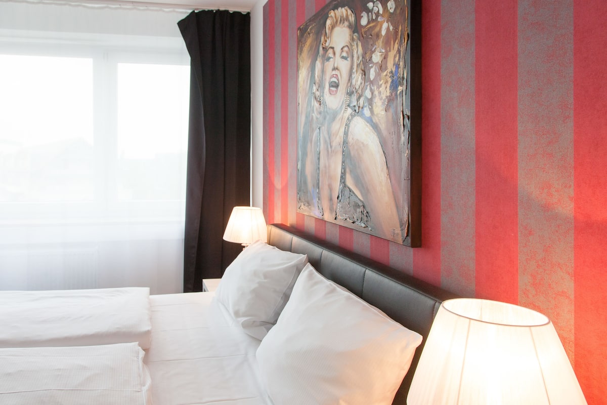 A hotel room with a bed, pillows, a lamp, and a painting on the wall.