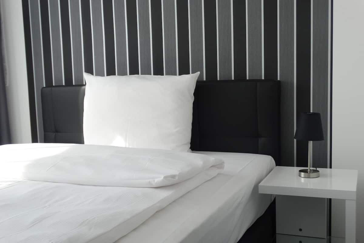 A neatly made bed with white linens, a black headboard, and a bedside table with a lamp.