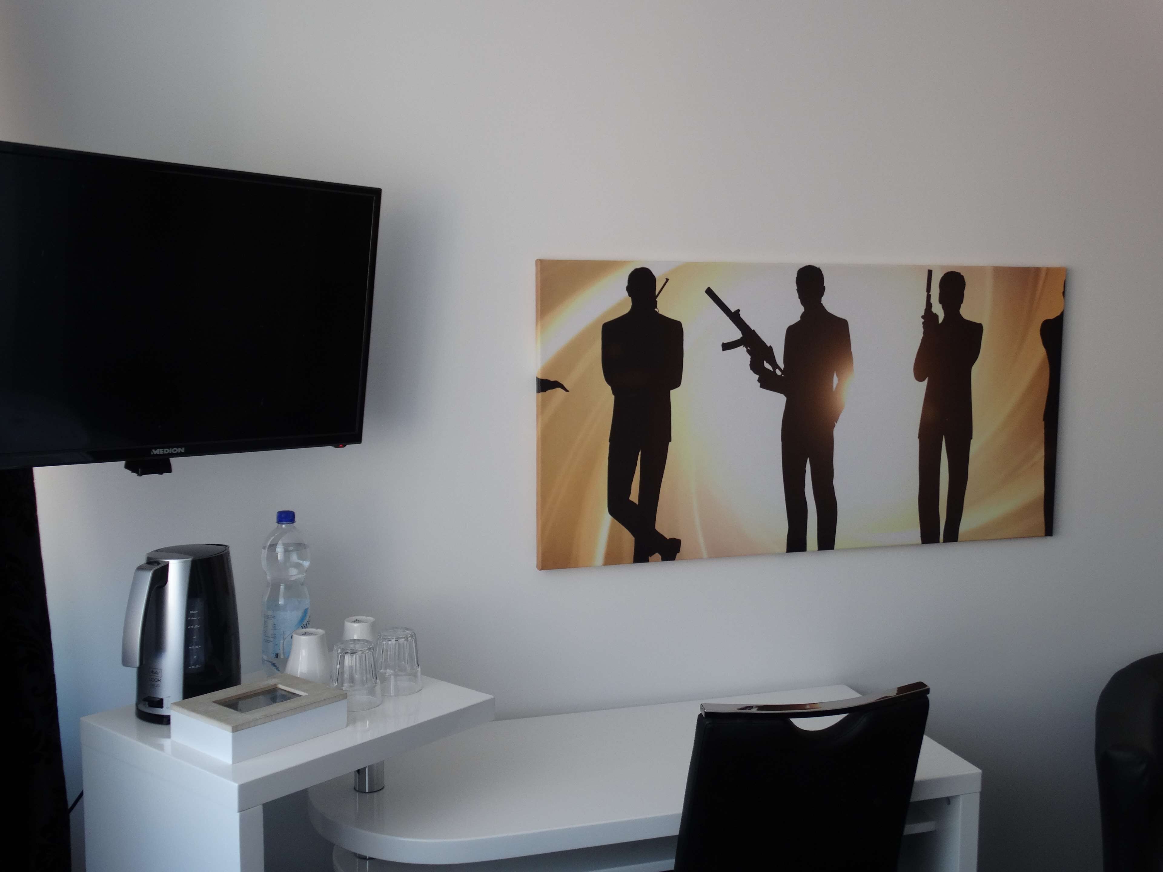 Habitació d'hotel amb televisió de pantalla plana, cafetera, ampolla d'aigua i un conjunt de vasos sobre una taula blanca.