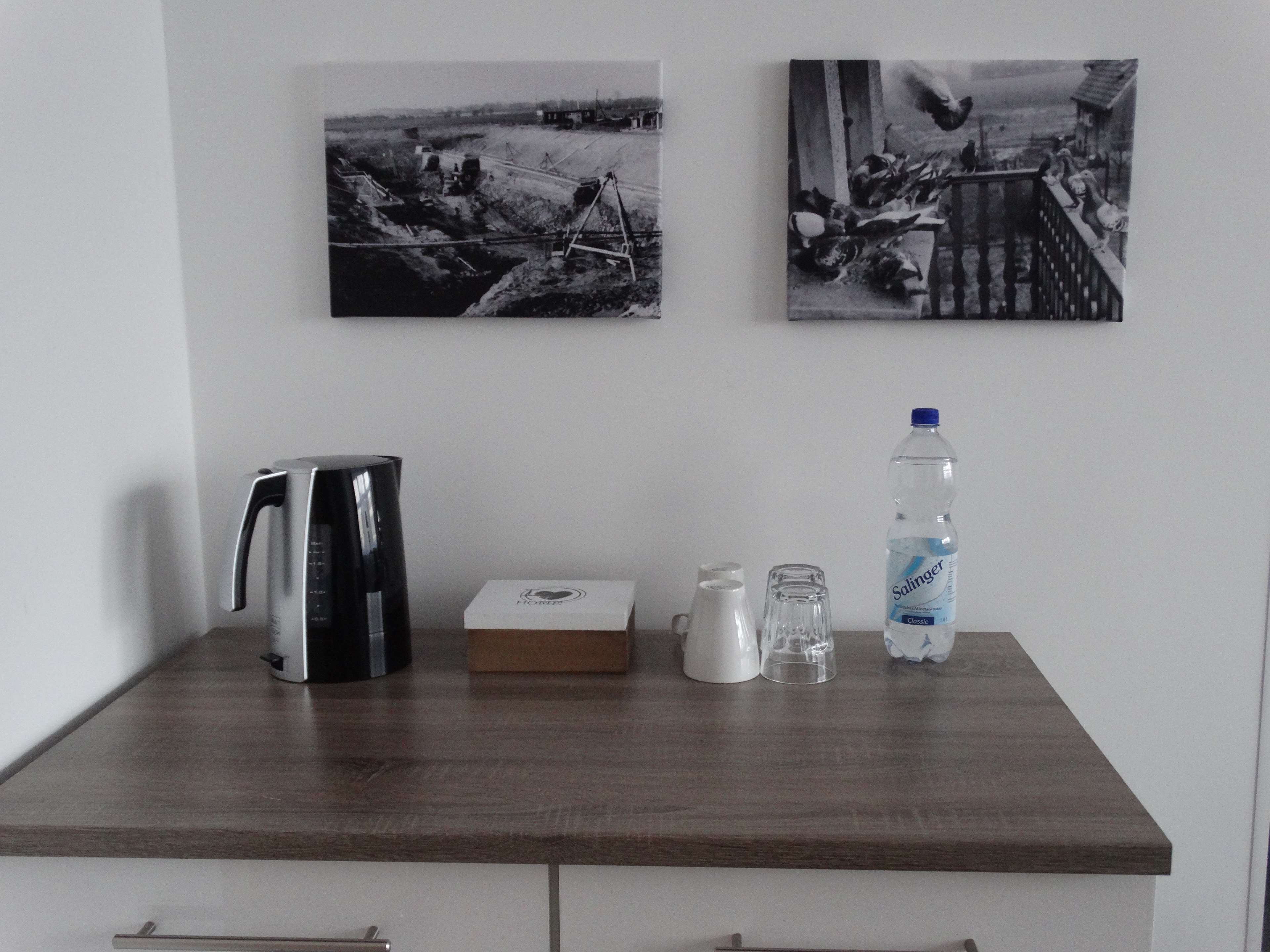 Ein Holztisch mit einer Kaffeemaschine, einer Schachtel, einem Glas und einer Wasserflasche.
